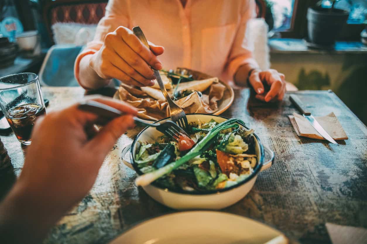 Woman taking some of her boyfriend's salad on lunch at a restaurant.