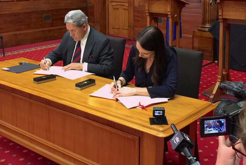 New Zealand Prime Minister-designate Jacinda Ardern signs official documents next to New Zealand First party leader Winston Peters