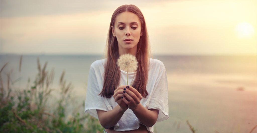 portrait of a brunette young woman  with a big dandelion on a background of warm sunset. summer, outdoors.