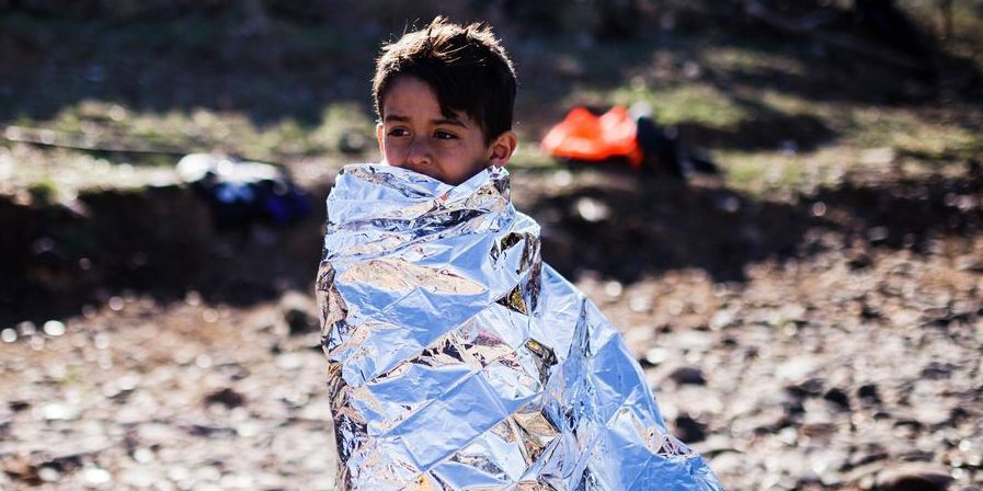 A young boy from Syria wrapped up in an emergency blanket to keep warm, stands on a beach after arriving at Lesbos with his family, having crossed the Aegean sea from Turkey in an inflatable boat.