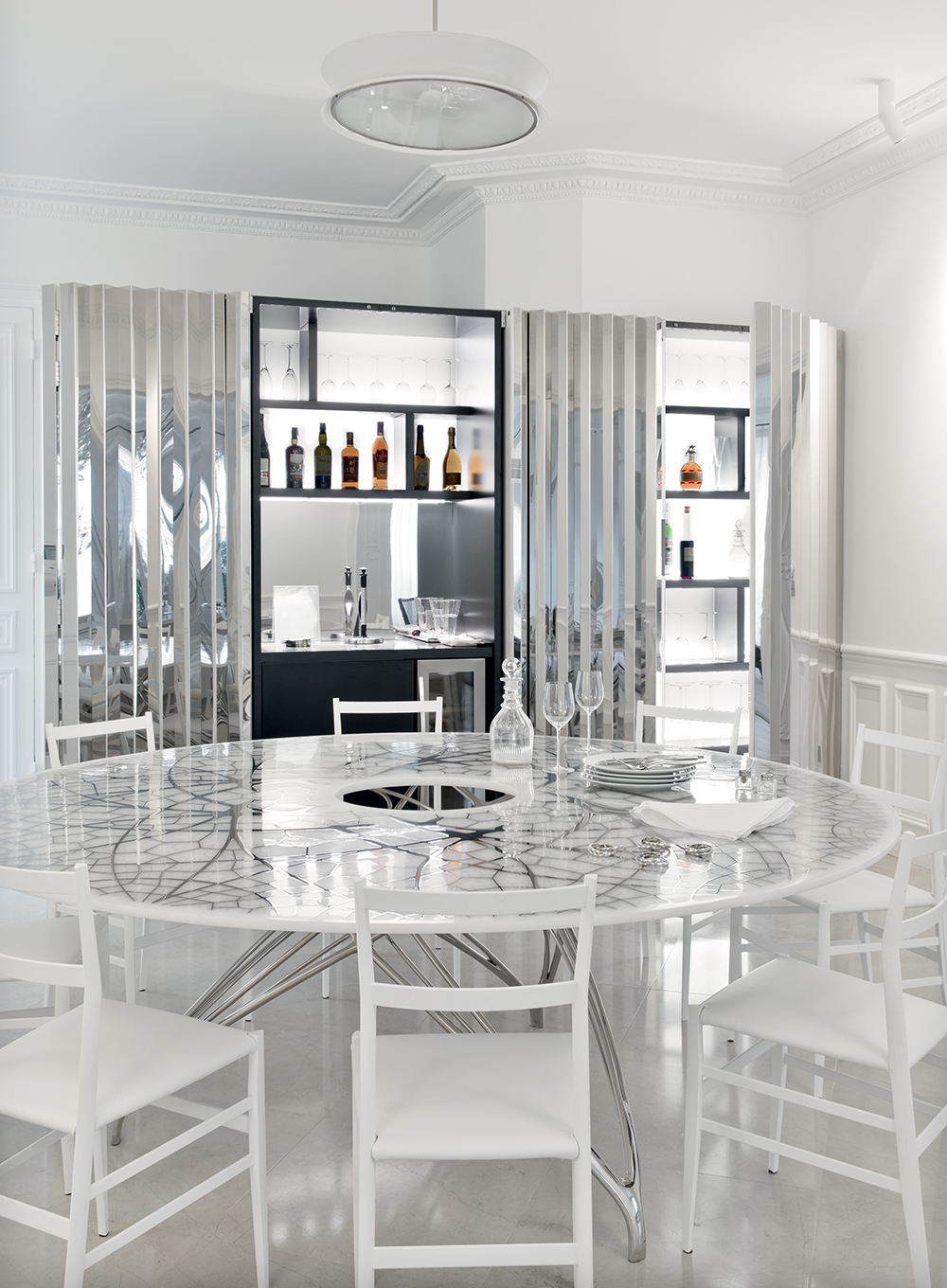 The custom-designed stainless steel cabinets conceal a bar, opened here in dramatic fashion, and keeps electronic equipment out of sight. A Joris Laarman table is paired with Gio Ponti “Superleggera” chairs.