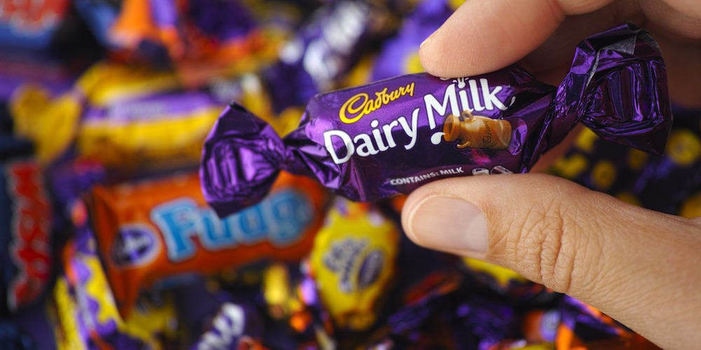 Paphos, Cyprus - November 27, 2015: Cadbury Dairy Milk candy in womans hand with background of Cadbury candies.