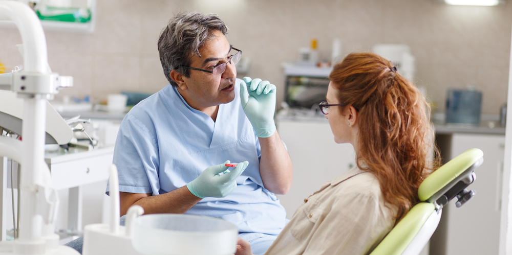 Senior male dentist in dental office talking with female patient and preparing for treatment.