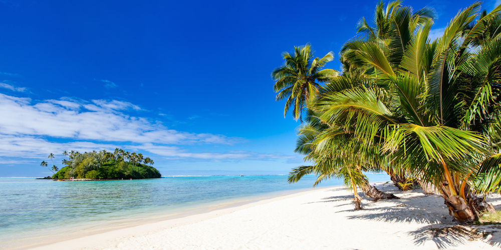 Beautiful tropical beach with palm trees, white sand, turquoise ocean water and blue sky at Cook Islands, South Pacific