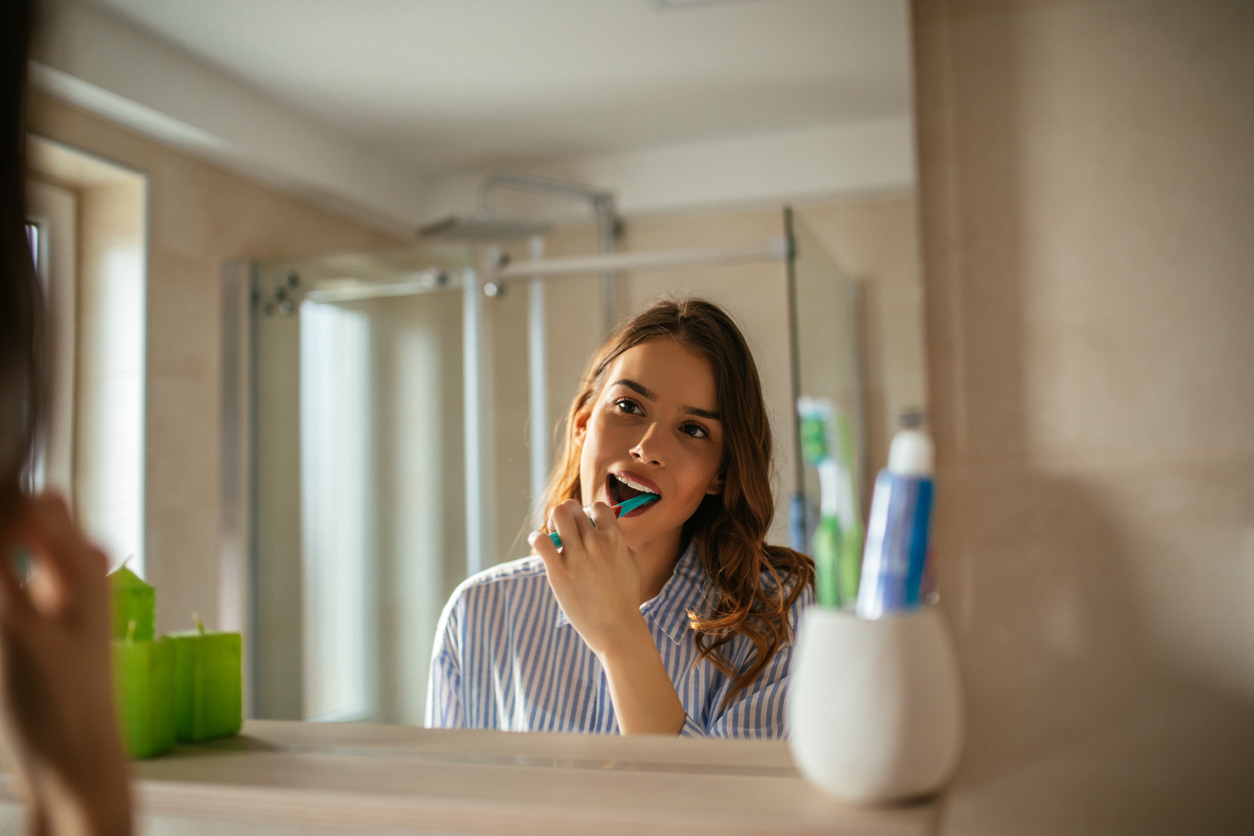 Portrait of a beautiful young woman brushing teeth in the bathroom.