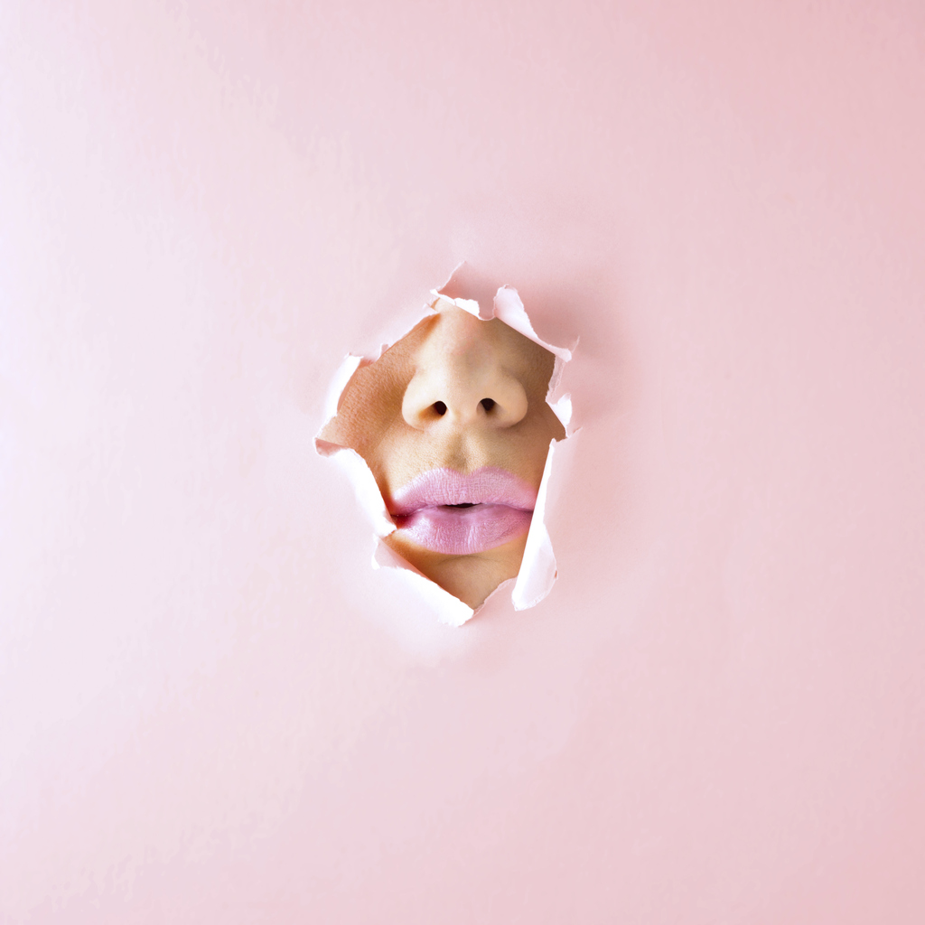 Creative concept photo of womans face and kiss lips painted with lipstick on pink paper background.