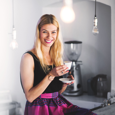 Portrait of a professional young woman barista sitting on a counter with a cup of coffee in a coffee shop.