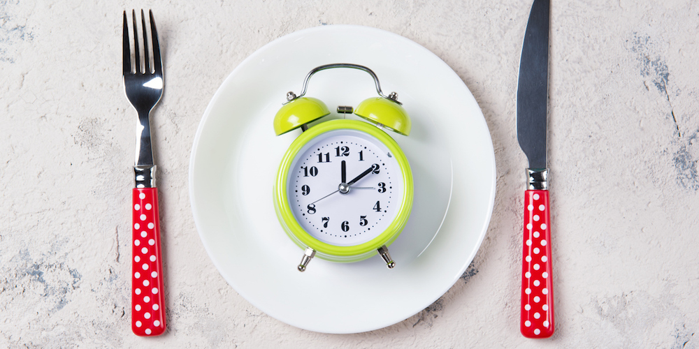 Green alarm clock with bells on the plate with fork and knife, lunch time concept, top view with copy space
