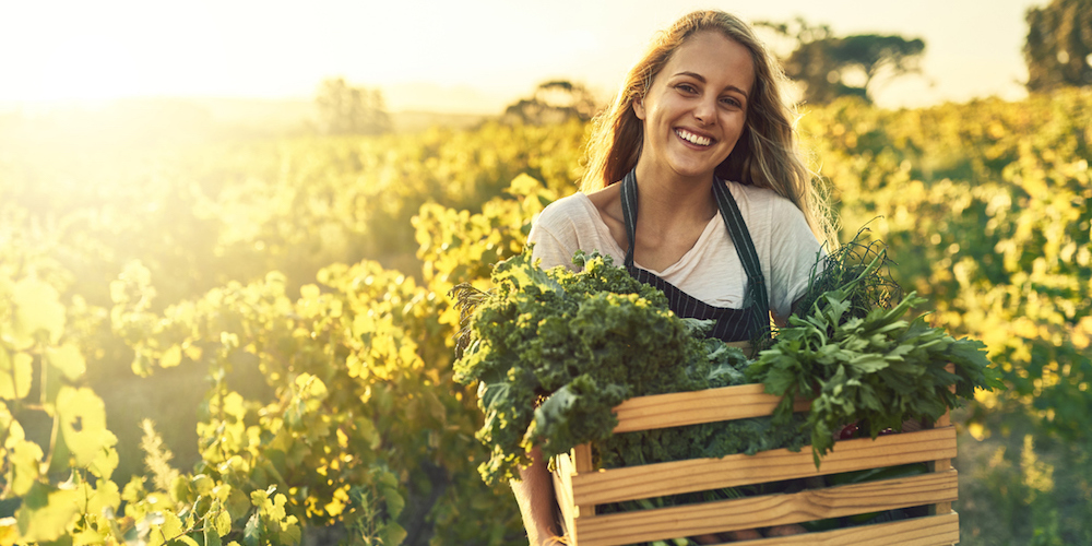Shot of a young woman holding a crate full of freshly picked produce on a farm