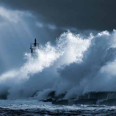 Big ocean wave over lighthouse against dramatic enhanced sky with sunbeams. Toned blue. North of Portugal.