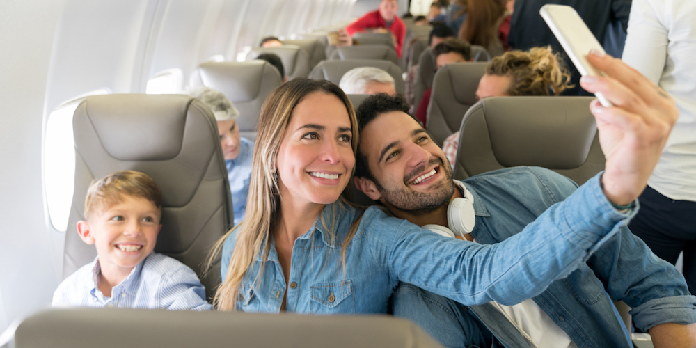 Happy family traveling by plane and taking a selfie with a cell phone while smiling - travel concepts