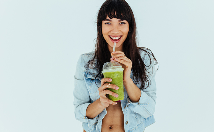 Portrait of beautiful woman drinking fresh green smoothie on white background. Smiling girl having a glass of fresh fruit juice.