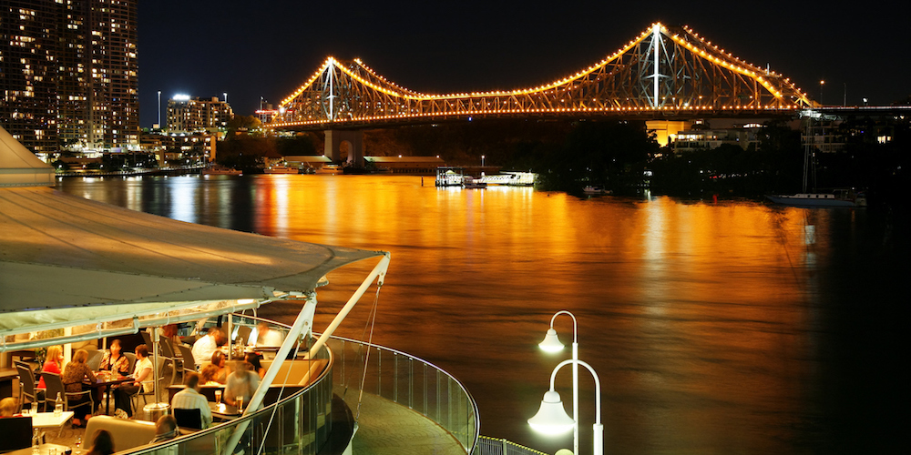 Brisbane, Australia - May 3, 2007: Several groups of people enjoy alfresco dining on the waterfront in Brisbane.  In the background, the lights of the famous Story Bridge reflect in the still waters of the Brisbane River.
