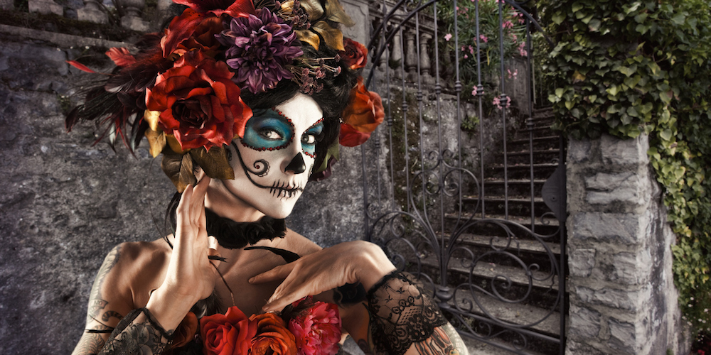 "A stock photo of a beautiful woman painted with sugar skull face in celebration of the Mexican holiday, Day of the Dead."