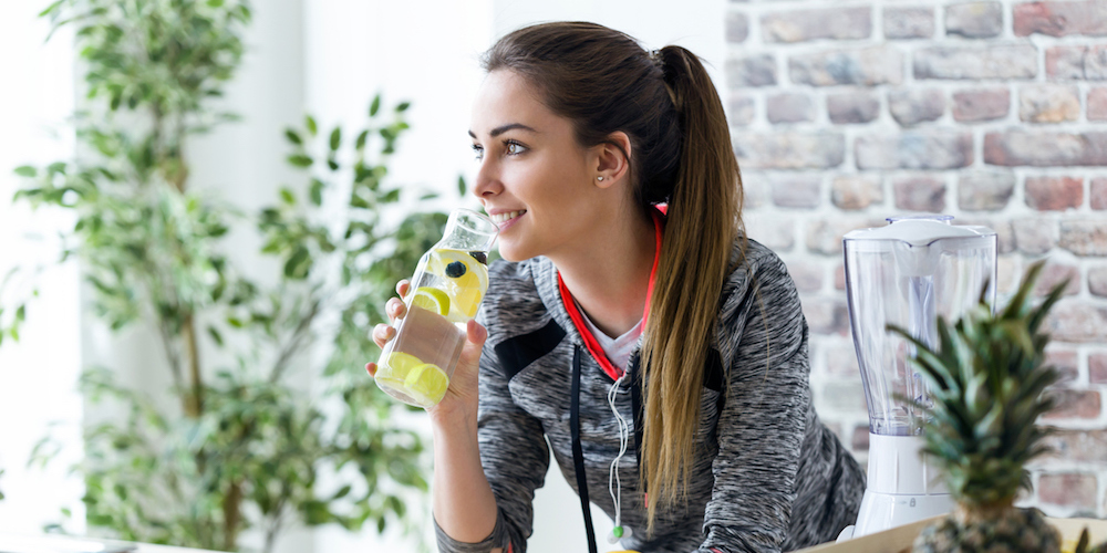 Shot of sporty young woman looking sideways while drinking lemon juice in the kitchen at home.