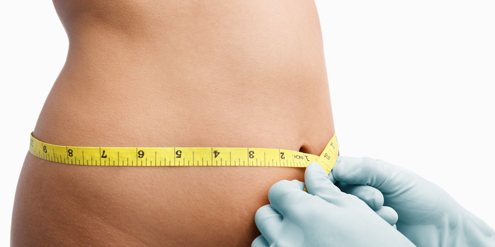 Female mid section being measure by doctor hand before liposuction over white background