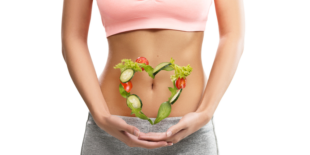 Fit, young woman holding a heart made out of vegetables over her abdomen