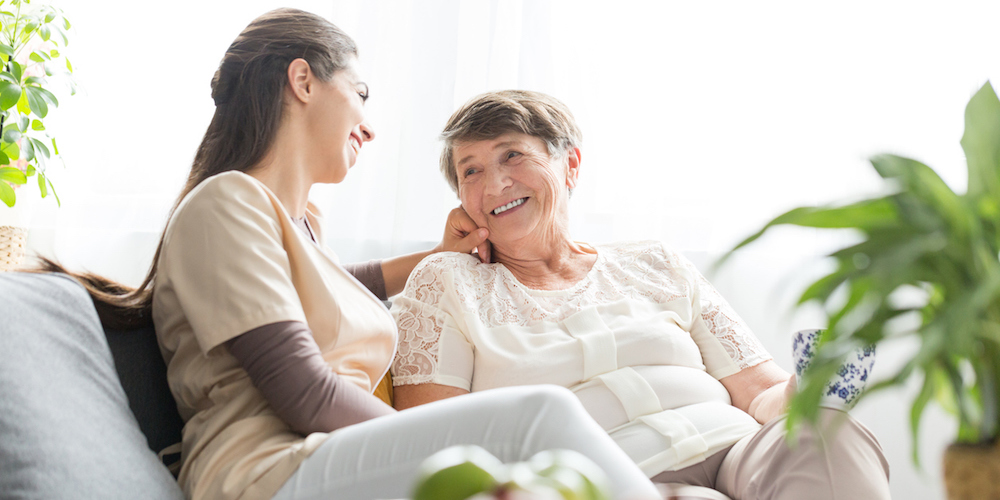Woman talking with happy elderly mother while sitting on sofa at home during meeting