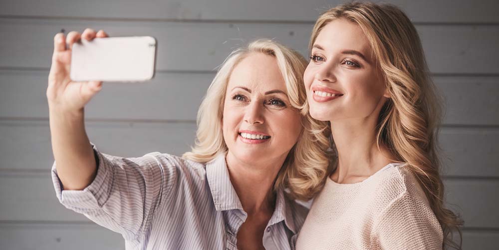 Beautiful senior mom and her adult daughter are doing selfie using a smart phone and smiling