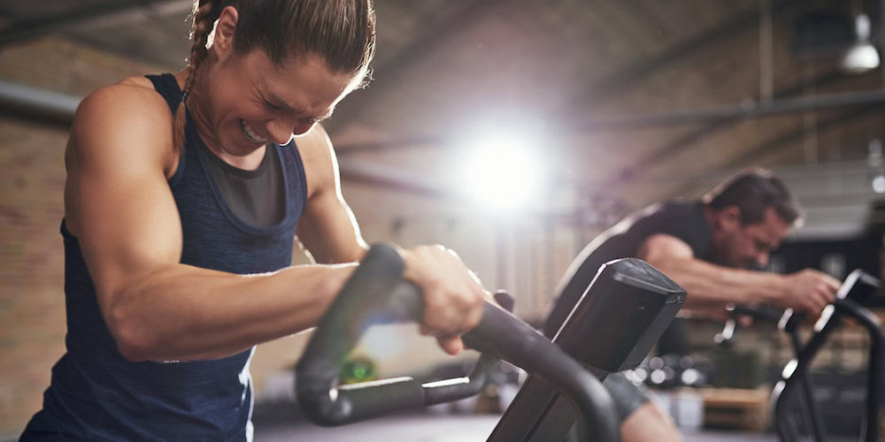 Young sportsmen having hard workout and grimacing on cycling machines in light gym.