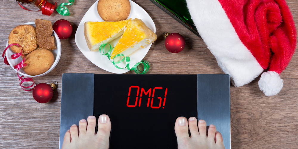 Female feet on digital scales with sign "omg!" surrounded by Christmas decorations, bottle, glass of alcohol and sweets. Consequences of overeating and unhealthy lifestile during holidays. Top view. (Female feet on digital scales with sign "omg!" surr