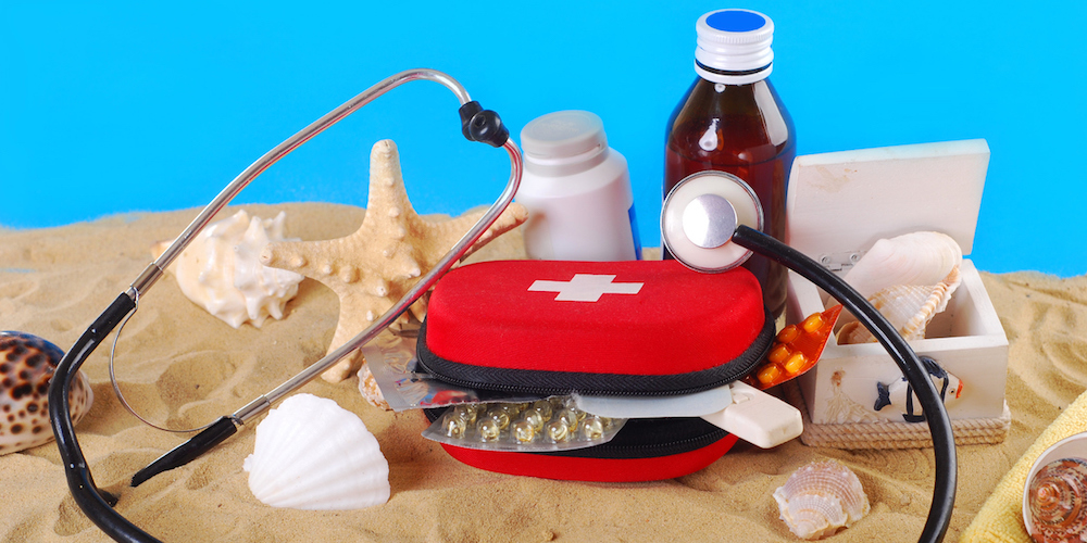 "first aid box with medicines,thermometer and stethoscope on the beach as healthy summer holiday concept"