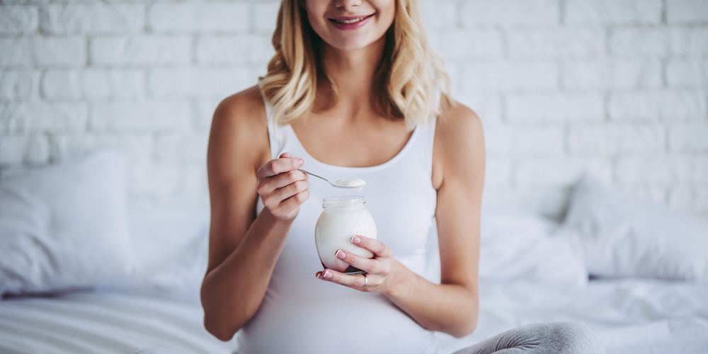 Cropped image of attractive pregnant woman is sitting in bed and eating yogurt. Healthy food concept. Last months of pregnancy. (Cropped image of attractive pregnant woman is sitting in bed and eating yogurt. Healthy food concept. Last months of pregn