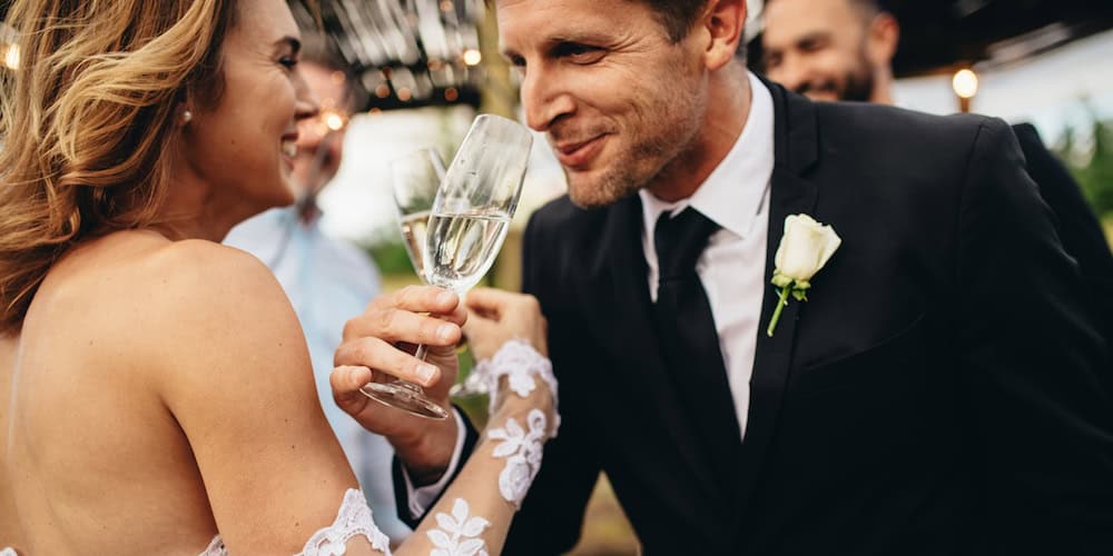 Newlyweds clinking glasses and enjoying romantic moment together at wedding reception outside. Bride and groom drinking champagne at wedding party. (Newlyweds clinking glasses and enjoying romantic moment together at wedding reception outside. Bride a