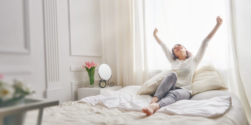Happy young woman enjoying sunny morning on the bed