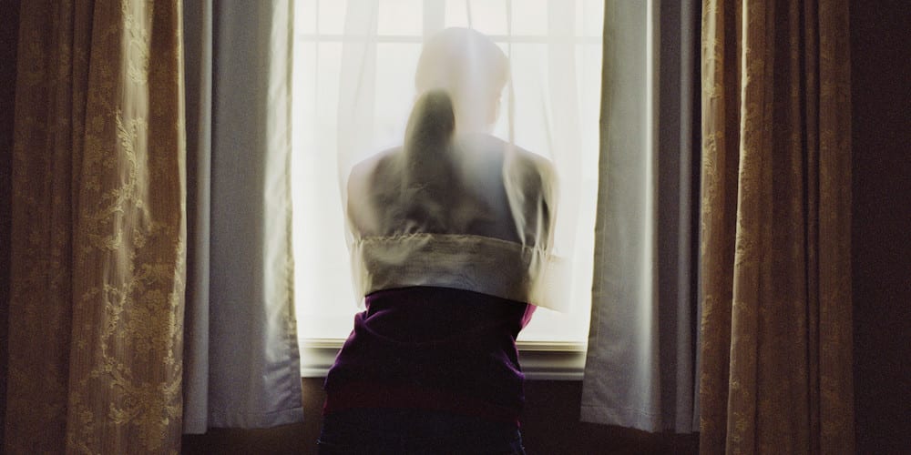 Young woman staring out bedroom window, rear view