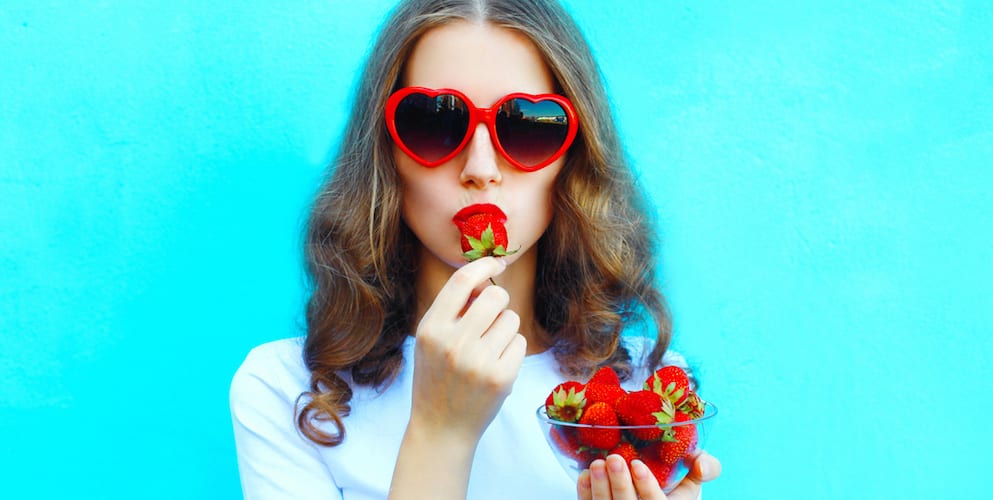 Portrait pretty woman with many strawberry over colorful blue background