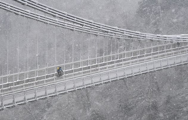 A person cycles over the Clifton Suspension Bridge and Avon Gorge in Bristol during snowfall in southwest Britain, February 1, 2019. REUTERS/Toby Melville     TPX IMAGES OF THE DAY - RC143FDA4750
