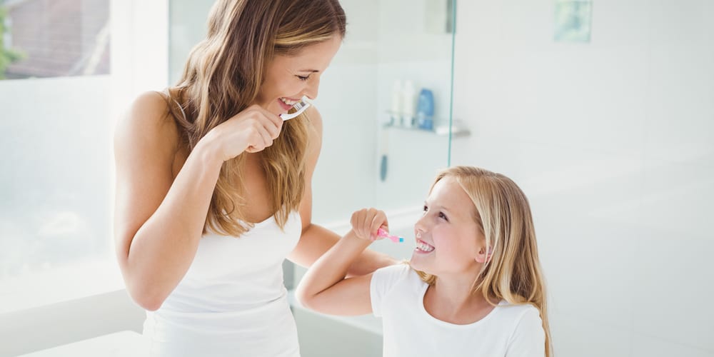 Smiling mother and daughter brushing teeth at home