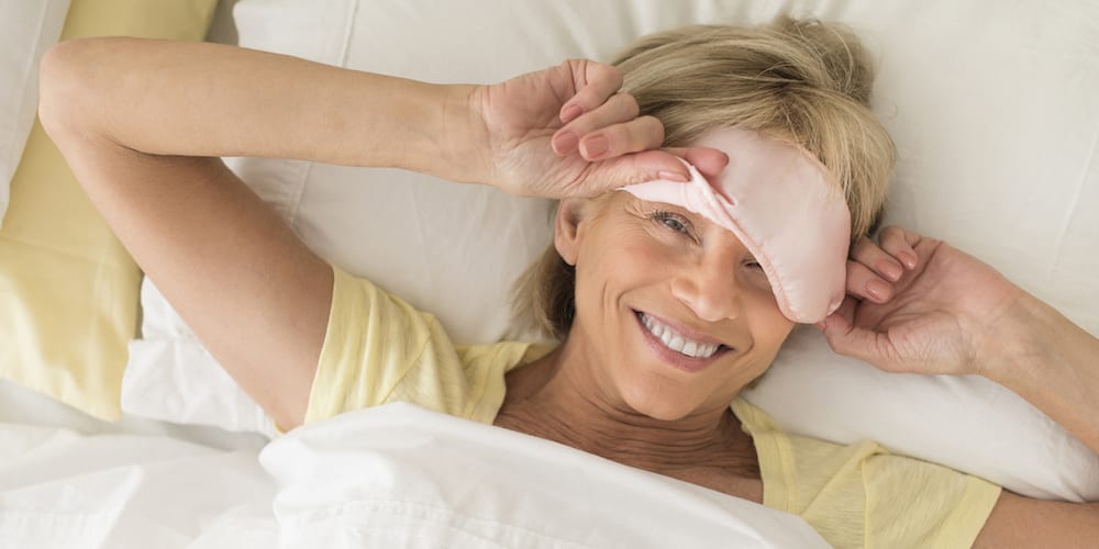 Happy Woman Wearing Sleep Mask On Bed
