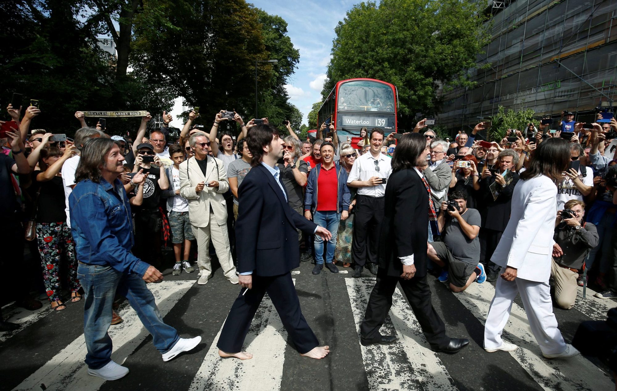 People take pictures as the Beatles cover band members walk on the zebra crossing on Abbey Road in London, Britain August 8, 2019. REUTERS/Henry Nicholls