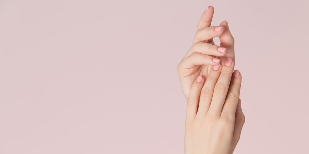 Woman hands with clean skin and nails with pink polish manicure on pink background. Nails care and beauty theme. Beauty background with copy space.
