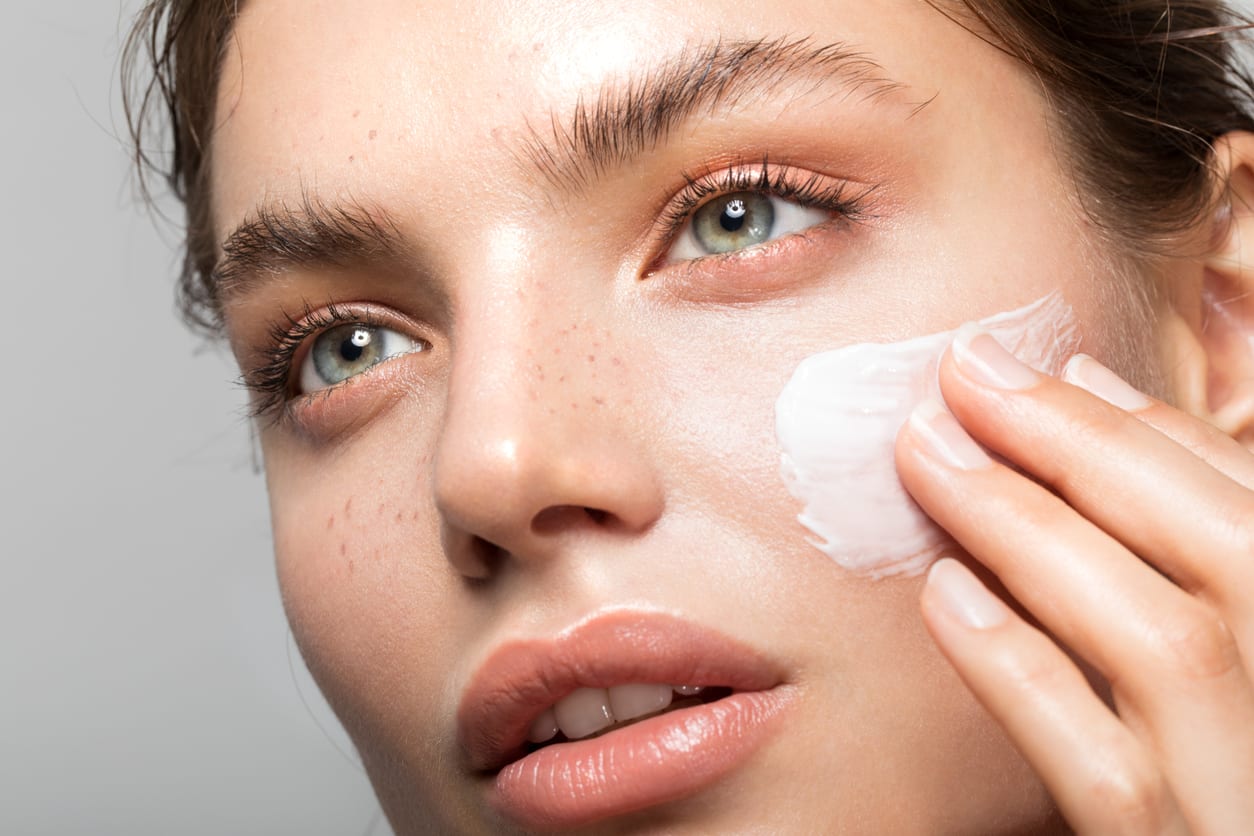 Close up studio shot of a beautiful woman with perfect skin, applying moisturizing cream