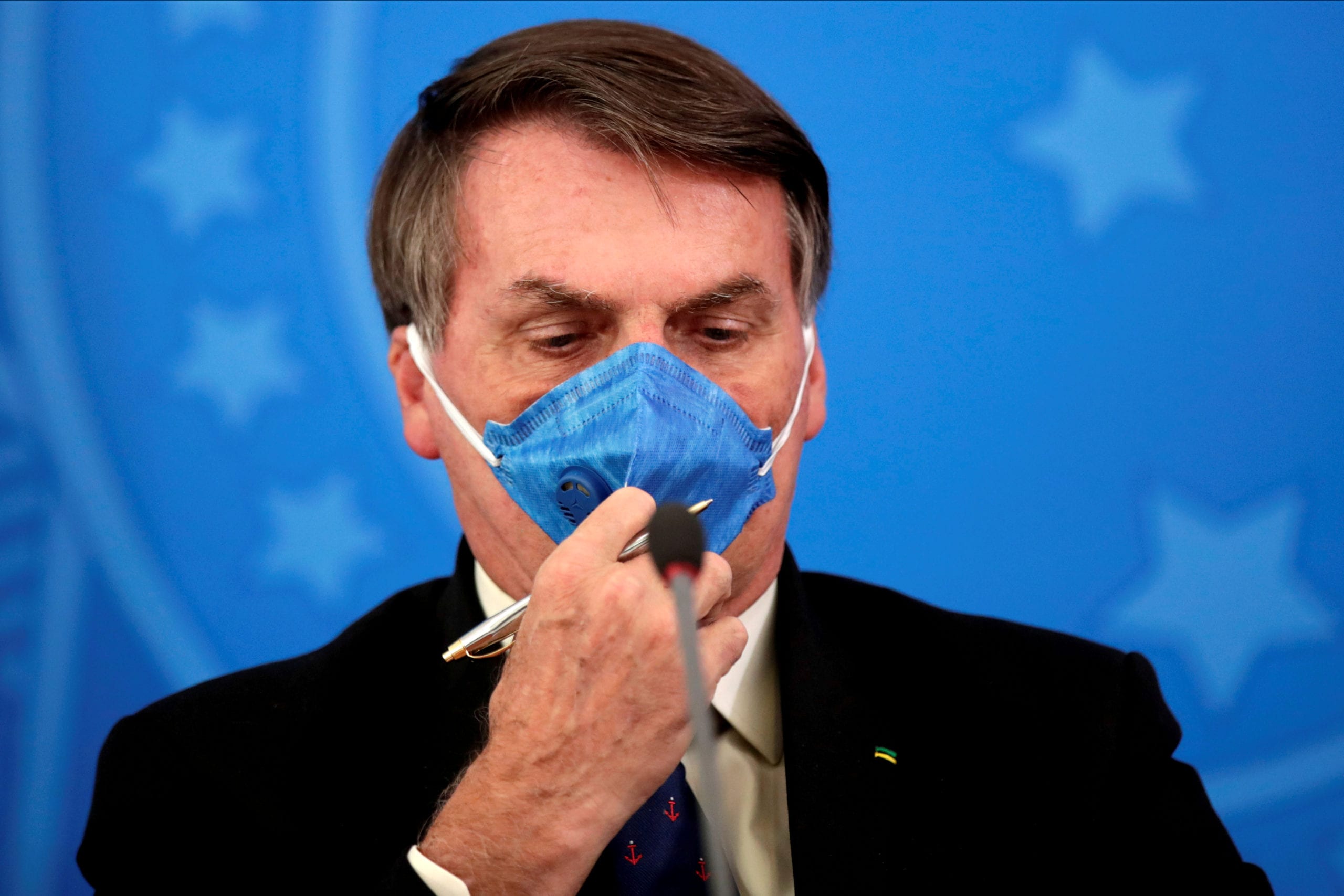 FILE PHOTO: Brazil's President Jair Bolsonaro adjusts his protective face mask at a press statement. REUTERS/Ueslei Marcelino/File Photo