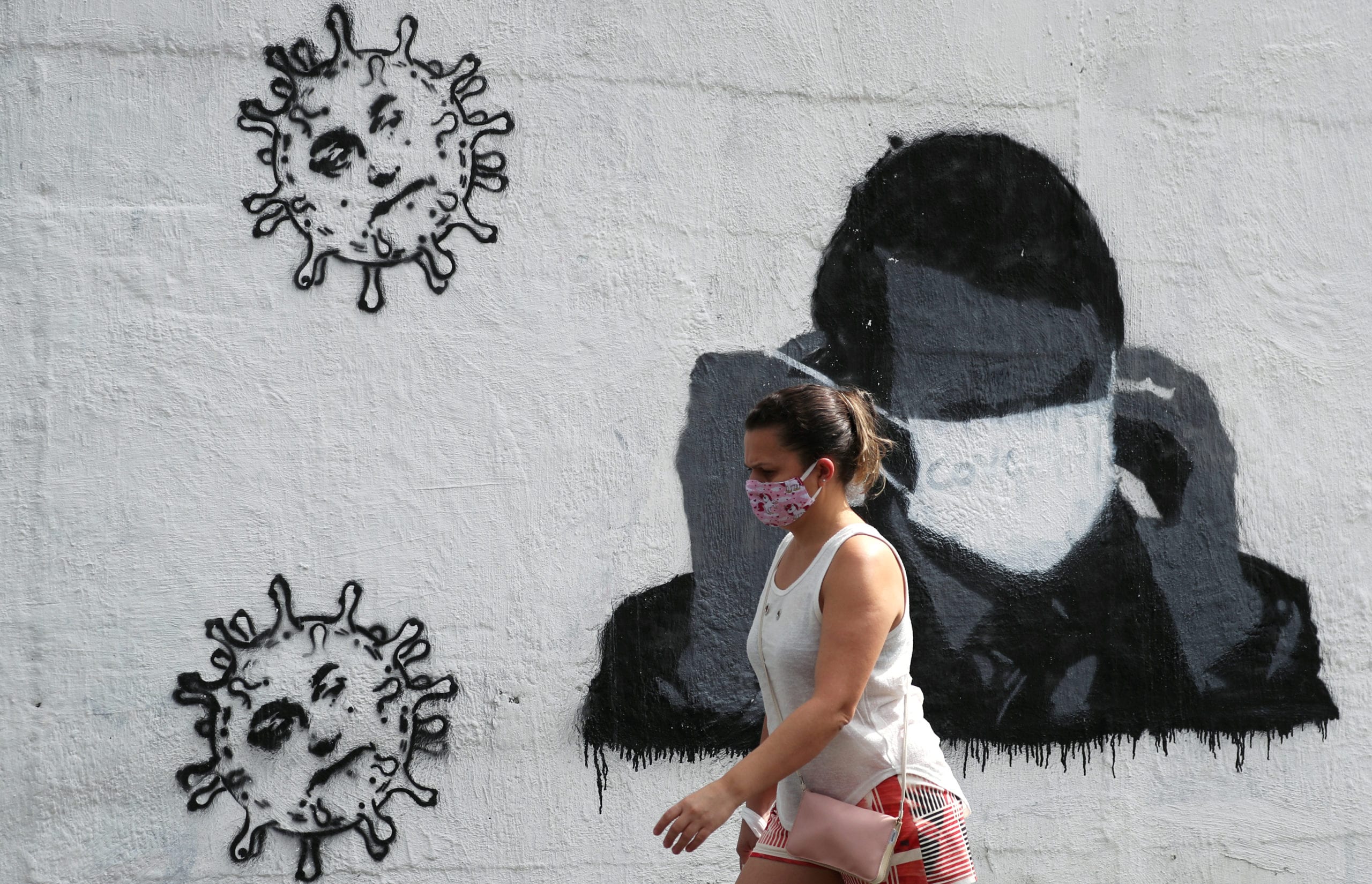 FILE PHOTO: A woman walks past graffiti depicting Brazil's President Jair Bolsonaro adjusting his protective face mask and viruses, amid the coronavirus  outbreak in Rio de Janeiro, Brazil July 2, 2020. REUTERS/Sergio Moraes/File Photo