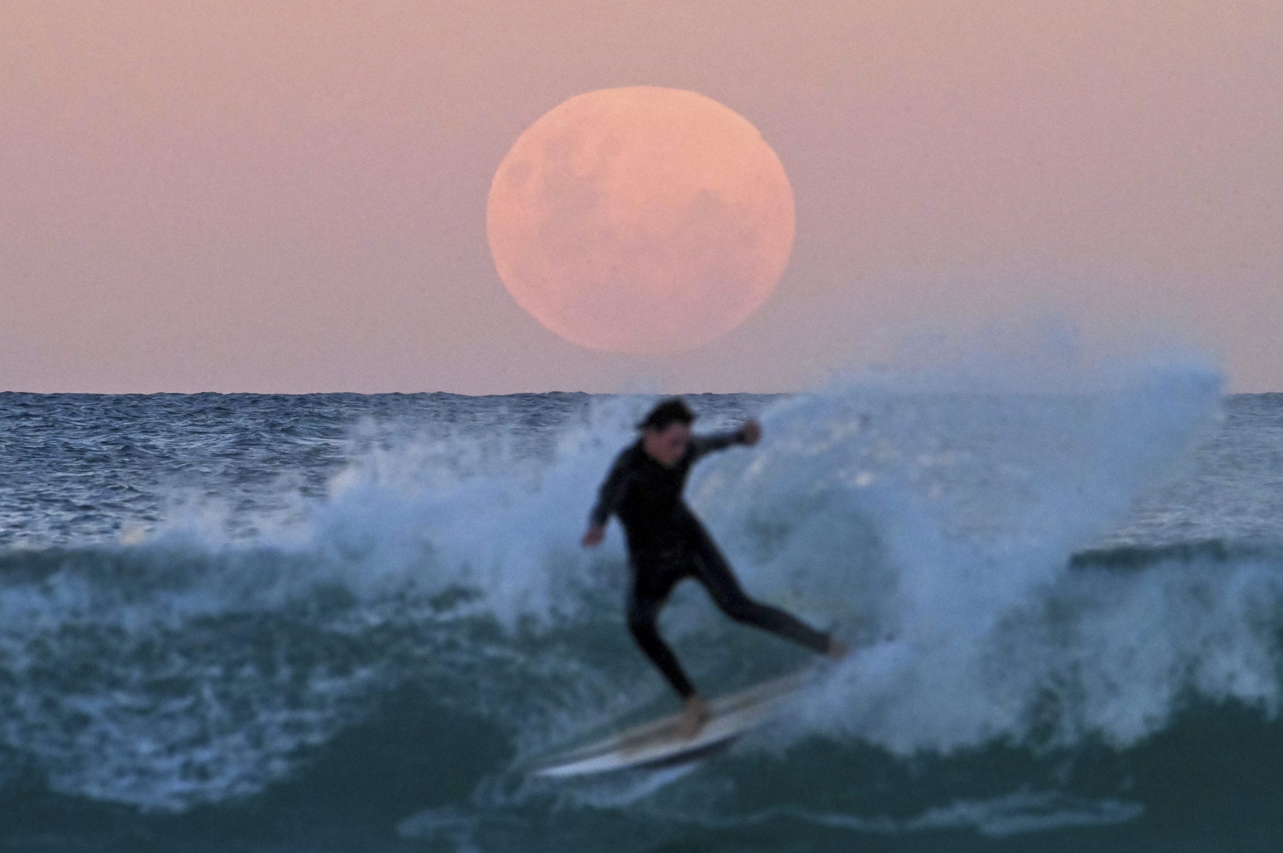 SYDNEY, AUSTRALIA - MAY 26: A surfer is seen as the "Super Flower Blood Moon" rises over the Pacific Ocean at Bondi Beach in Sydney, Australia on May 26, 2021. The "Super" moon observed in May is often defined as "flower moon" as well, mainly due to association with flowers blooming at this time of year. During the eclipse, the moon turns into a deep blood-red color, known as "blood moon." This celestial incident -- known as "Super Flower Blood Moon" -- is the only full lunar eclipse of this year. (Photo by Steven Saphore/Anadolu Agency via Getty Images)