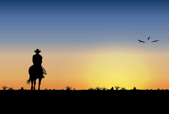 Silhouette of lonesome cowboy riding horse at sunset
