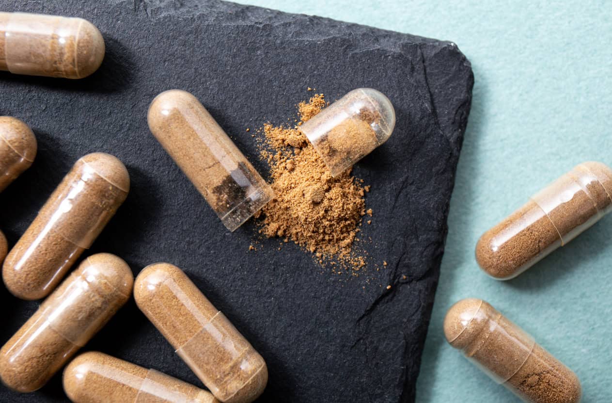 Withania somnifera known as ashwagandha. Ashwagandha root powder supplement capsules on black background.