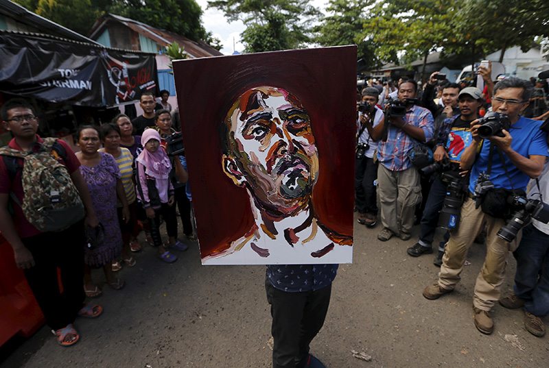 A man carries a self-portrait painted by Australian death row prisoner Myuran Sukumaran as he leaves Wijayapura port in Cilacap
