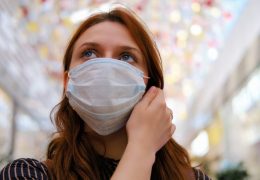 A young woman is considering whether to remove the medical mask after the end of the quarantine due to the coronavirus. Portrait of a girl after the flu virus epidemic, close-up