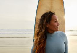 Smiling mature woman standing on a beach with her surfboard
