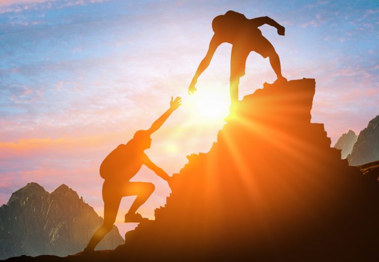 Man is giving helping hand. Silhouettes of people climbing on mountain at sunset. Help and assistance concept. Silhouettes of two people climbing on mountain and helping.