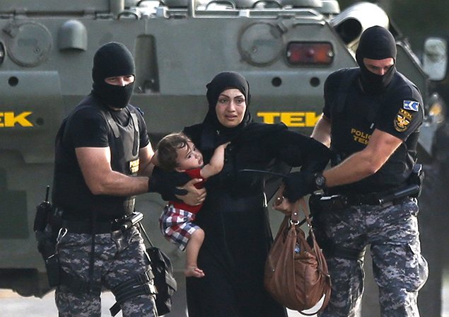 Two Hungarian riot policemen escort a migrant woman and her child in Roszke, Hungary.
REUTERS/Dado Ruvic 