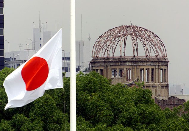 The Japanese national flag flutters at half-mast in the foreground of the atomic bomb dome at the Hiroshima Peace Memorial Park. REUTERS/Kimimasa Mayama.