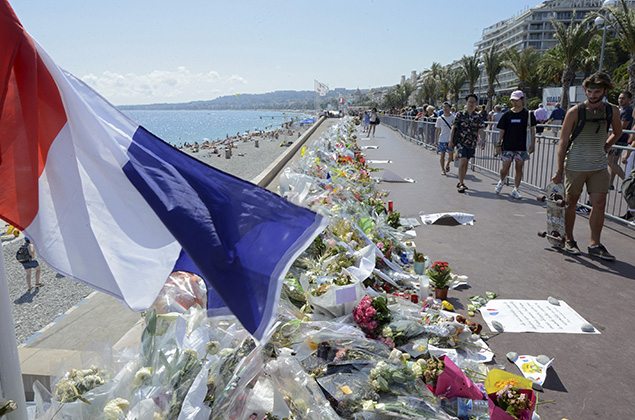 People walk past flowers left in tribute at a makeshift memorial to the victims of the Bastille Day truck attack near the Promenade des Anglais in Nice. REUTERS/Jean-Pierre Amet.
