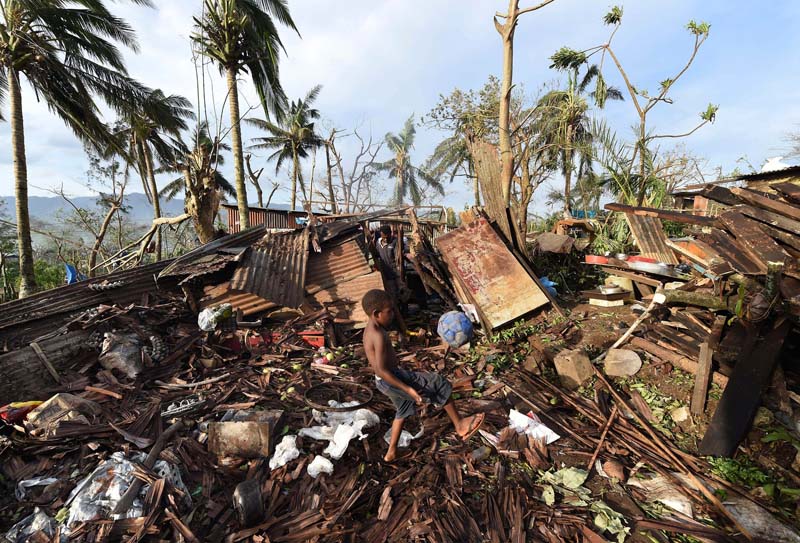 A boy called Samuel kicks a ball as his father Phillip searches through the ruins of their home which was destroyed by Cyclone Pam in Port Vila